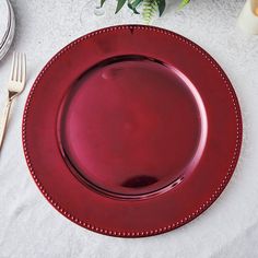 a red plate sitting on top of a white table cloth next to a fork and knife