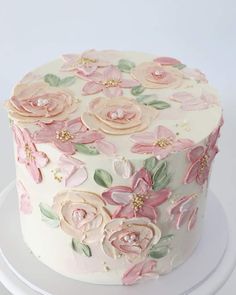 a white cake decorated with pink flowers and green leaves on a plate in front of a white background