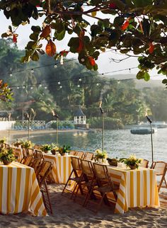 tables set up on the beach with yellow and white striped tablecloths