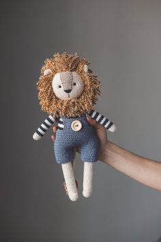 a hand holding a knitted lion doll with stripes on it's shirt and pants