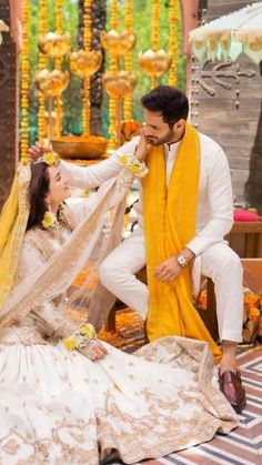 a man kneeling down next to a woman in a white and yellow wedding dress on the ground