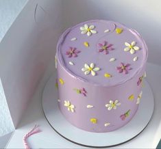 a purple cake with white and yellow flowers on it sitting in a box next to a string