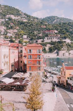 the town is surrounded by mountains and trees, with boats docked on the water in the distance