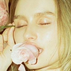 a woman is smelling a pink flower with her eyes closed and tongue out to the side