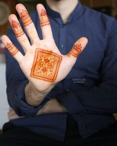 a man is holding his hand painted with red and orange hendi prints on it