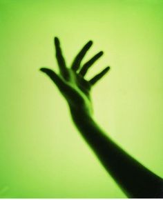 a person's hand reaching up into the air in front of a green background