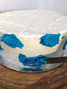 a white cake with blue icing sitting on top of a wooden board next to a knife