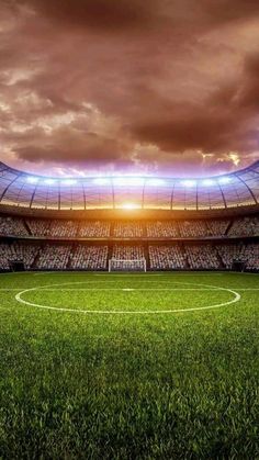 a soccer field with the sun setting in the sky and clouds above it, as well as an empty stadium