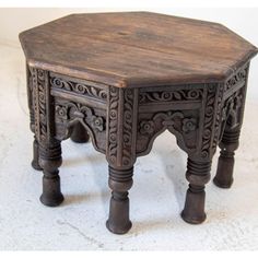 an old wooden table with carved designs on the top and bottom, sitting on a white surface