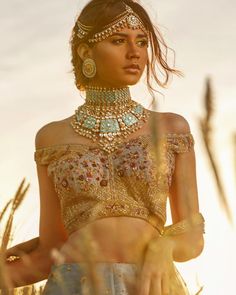 a woman in a gold and white outfit with jewelry on her head, standing in tall grass