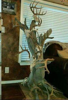 a fake tree with antlers on it in front of a window and a couch