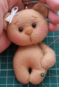 a hand holding a small teddy bear on top of a green table with scissors and thread