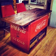 an old coca - cola cooler table in the middle of a kitchen with red chairs