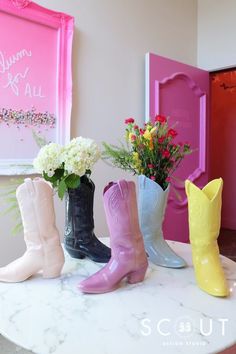 four pairs of cowboy boots sitting on top of a marble table with flowers in them