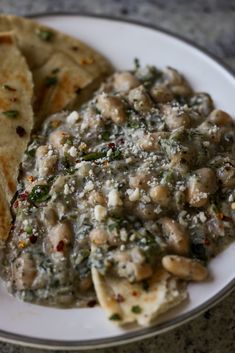 a white plate topped with tortilla shells covered in cheese and sauce next to pita bread