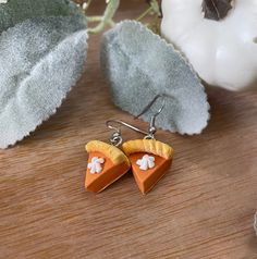 two slices of pie shaped earrings sitting on top of a wooden table next to leaves