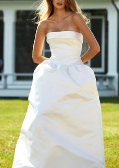 a woman in a white wedding dress standing on the grass with her hands on her hips