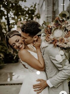 a bride and groom kissing in front of a building with greenery on the side