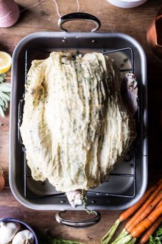 an uncooked chicken in a roasting pan surrounded by carrots and other vegetables