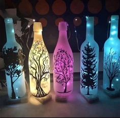 lighted wine bottles with trees on them sitting in front of a wall