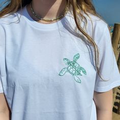 This is a personalised, white embroidered t-shirt with our Turtle image on the front.  Please select the personalisation tab below to choose the thread colour of your choice and to add any matching colour text to the arm up to a max of 12 characters, such as initials, a memorable beach, a name or a location.   A great addition to your wardrobe or as a gift the high quality great fitting organic unisex t-shirt is perfect for any occasion, not only is it organic but it is also PETA Vegan approved. It's a must-have for anyone who loves the sun, sand, and surf! This ultra-comfy and stylish t-shirt is the perfect gift for beach enthusiasts, ocean lovers, or anyone who appreciates a one-of-a-kind piece of clothing that brings back memories of sun-soaked days, sea or lovely summer holidays. Make Turtle Image, Embroidered Turtle, Turtle Images, Colour Text, Turtle Gifts, Summer Holidays, Embroidered Tshirt, Significant Other, Sun Kissed