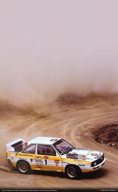 a rally car driving down a dirt road in the desert with dust coming from its tires