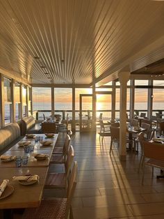 an empty restaurant with the sun setting over the ocean in the backgrouds