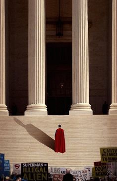 a person in a red cloak standing on the steps of a building with protest signs