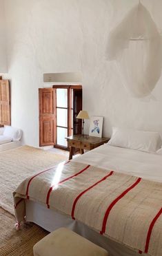 two beds in a room with white walls and wooden doors, one has a red stripe on the bed