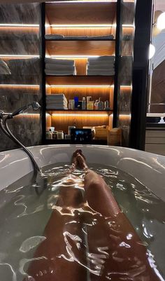 a person laying in a large bathtub filled with water next to a bookshelf