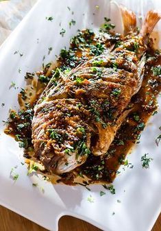 a white plate topped with fish covered in sauce and garnished with parsley