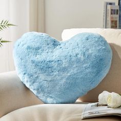 a blue heart shaped pillow sitting on top of a couch next to a white rose