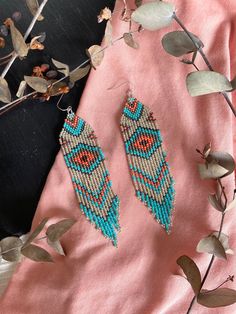 two pairs of beaded earrings on top of a pink cloth next to some leaves