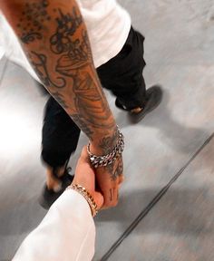 two people holding hands with tattoos on their arms and one is wearing a white shirt