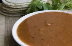 a white bowl filled with soup next to some pita bread and cilantro