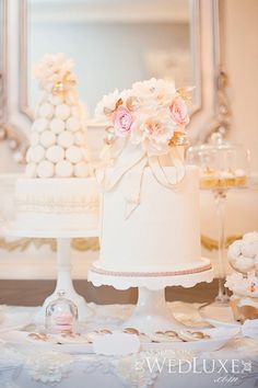 a white wedding cake with pink flowers on top and other desserts in the background