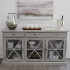 a dining room buffet table with plates and cups on it, next to a painting