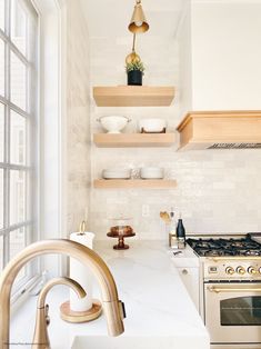 a kitchen with white counter tops and wooden shelves above the stove top, next to a window