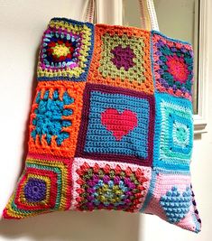 a multicolored crocheted tote bag hanging from a hook on a wall