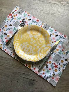 a yellow and white flowered placemat on a wooden table with a fork and knife