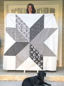 a black dog laying in front of a large quilt