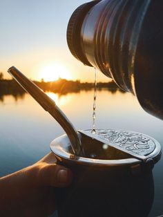 a person is pouring water into a metal bowl on the edge of a body of water