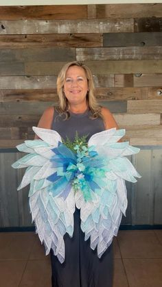 a woman standing in front of a wooden wall holding a blue and white flower arrangement