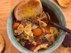 a bowl of soup with noodles, carrots, meat and bread on the side