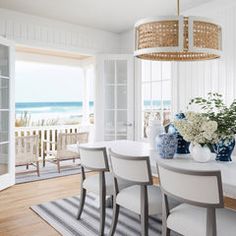 a dining room table with chairs and vases on top of it next to the ocean