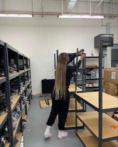 a woman with long blonde hair standing in a room filled with shelves and shelving