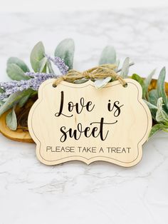 a wooden sign that says love is sweet please take a treat next to some flowers