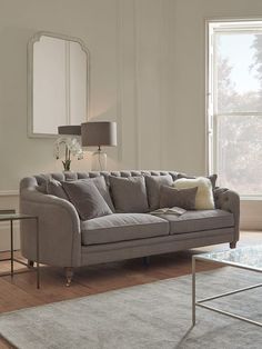 a living room with a gray couch and two tables in front of the large window