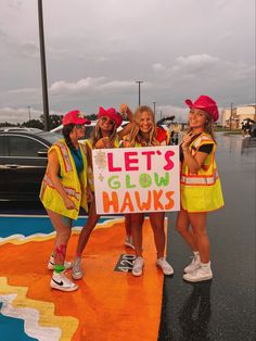 three girls in yellow safety vests holding a sign that says let's glow hawks