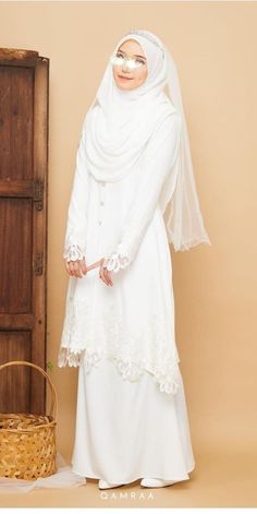 a woman wearing a white hijab standing in front of a wooden door and basket